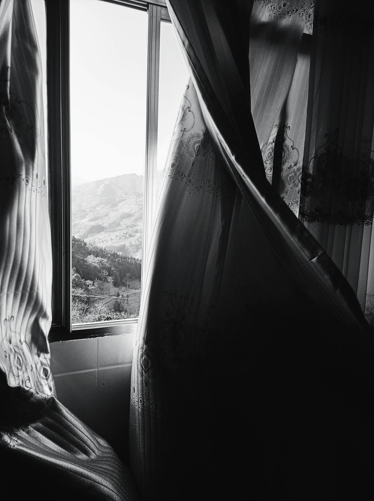 Light breaking into a dark room through a parted curtain, mountains beyond